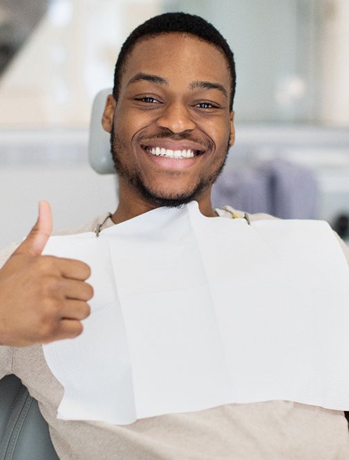 Man sitting in dental chair smiling and giving thumbs up